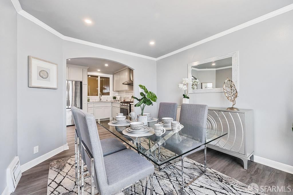 Staged dining room with a glass table and gray chairs, opening to a white kitchen.