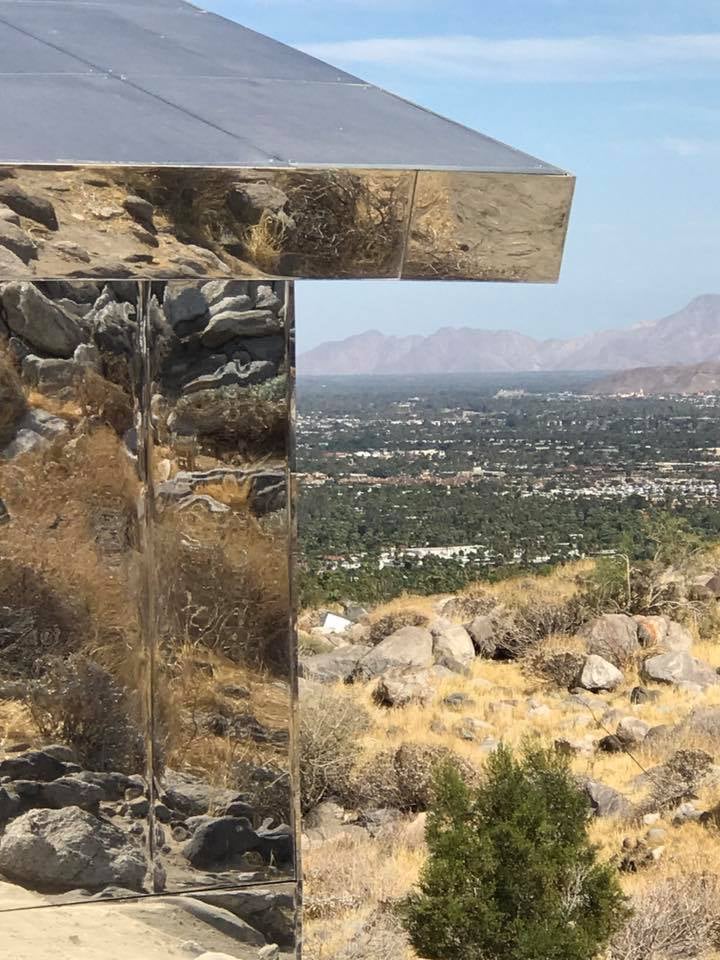 Mirrored Mirage installation reflecting rocky desert terrain, with a valley and mountains beyond.