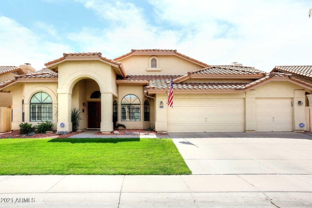 Single-story stucco home with an arched entryway, tiled roof, three-car garage, and green lawn.
