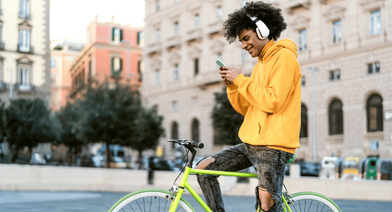 Young man with headphones checks his phone beside a bright green bicycle downtown.