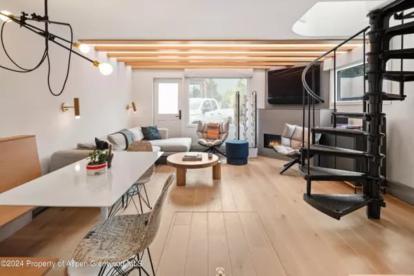 Modern living room with exposed ceiling beams, light wood floors, and a black spiral staircase.