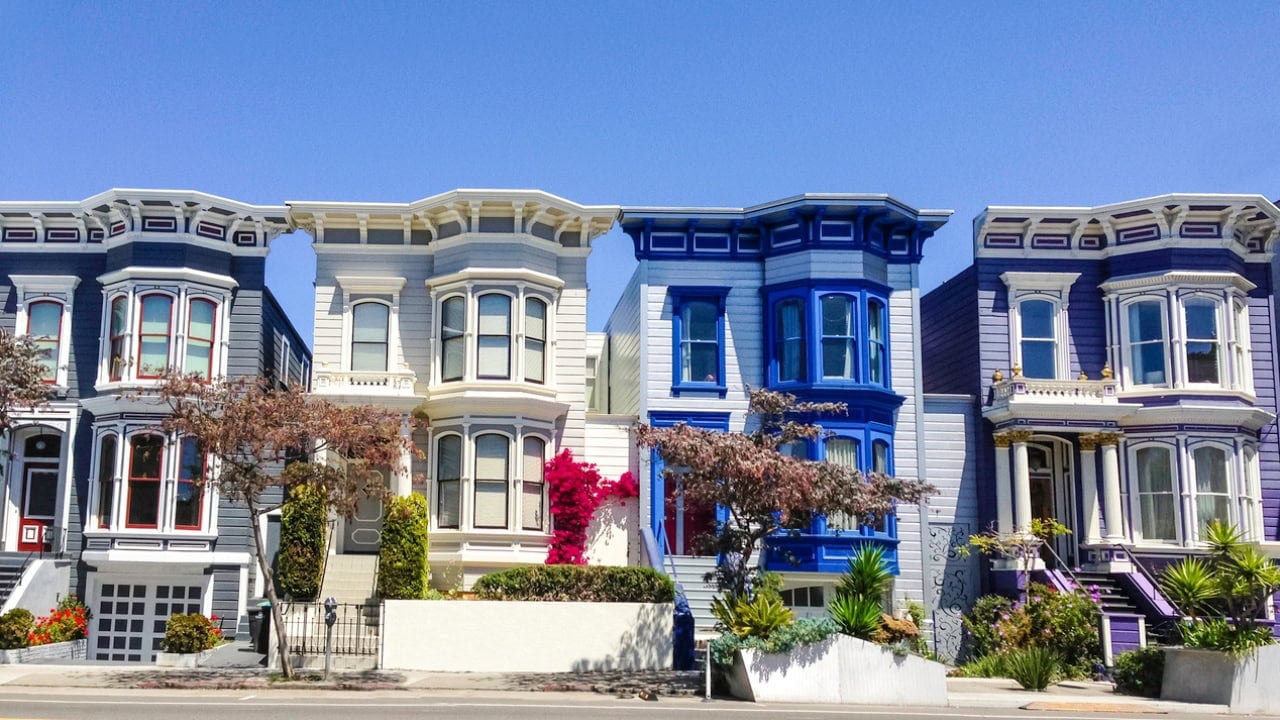 Colorful Victorian homes with ornate trim and bay windows along a sunny street.