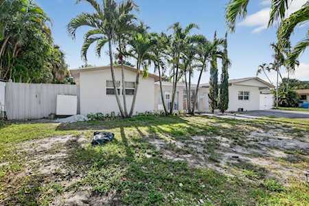 White single-story home with a patchy lawn, tall palm trees, and a white fence.