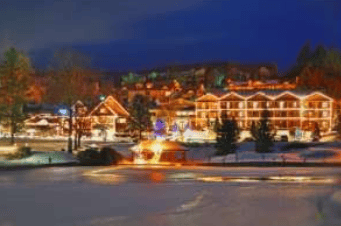 Snow-covered mountain resort village with warmly lit lodge buildings at night.