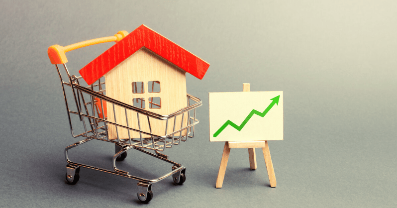 Miniature house in a shopping cart beside a rising green market chart.