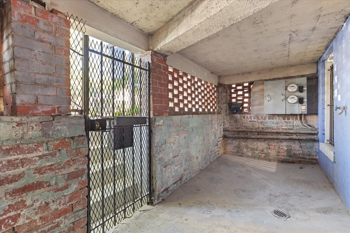 Covered utility area with exposed brick, a metal security gate, and electrical meters.
