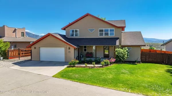 Two-story Rifle home with an attached garage, covered porch, flower beds, and green lawn.