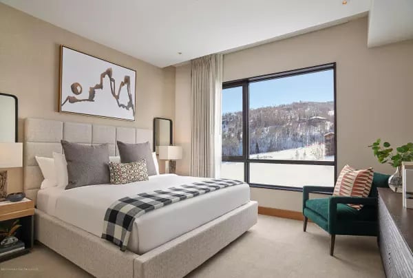 Furnished bedroom with a large window overlooking a snowy, wooded mountain.
