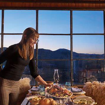 Woman arranging a meal at a window-side table with mountain views.