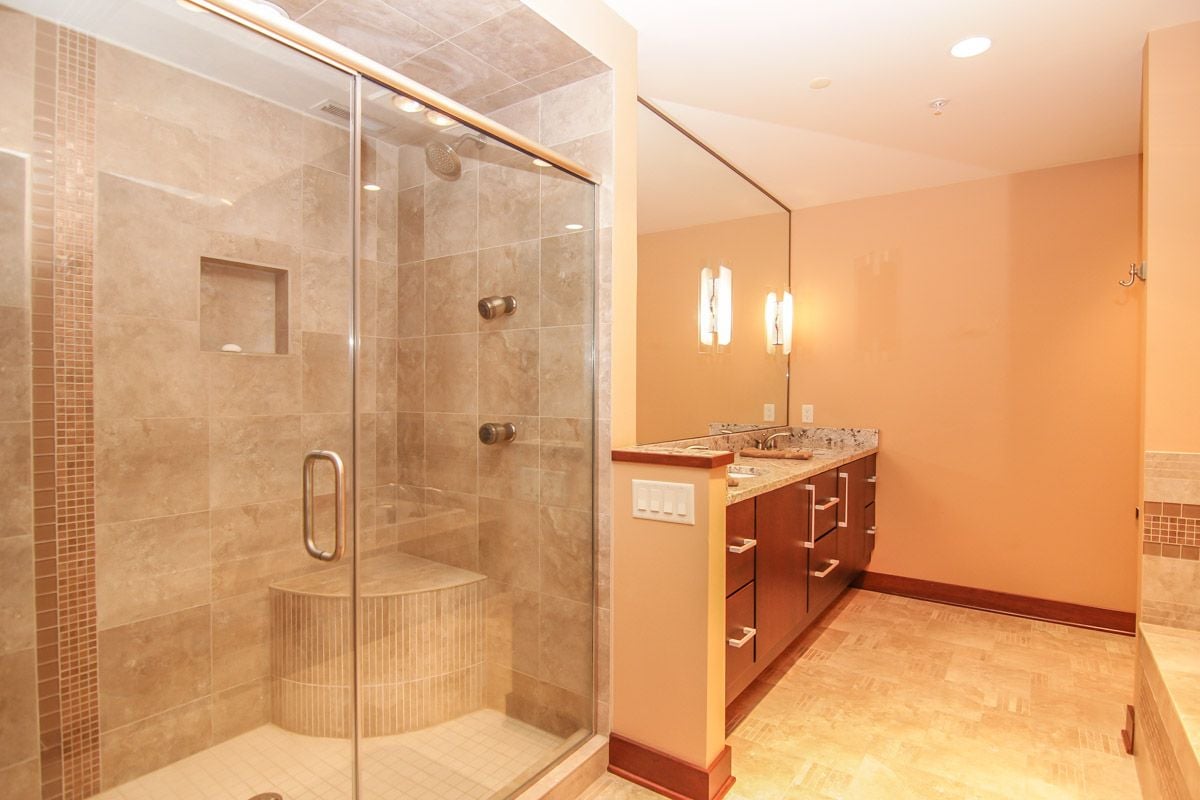 Bathroom with a glass-enclosed tiled shower and long dark-wood vanity.