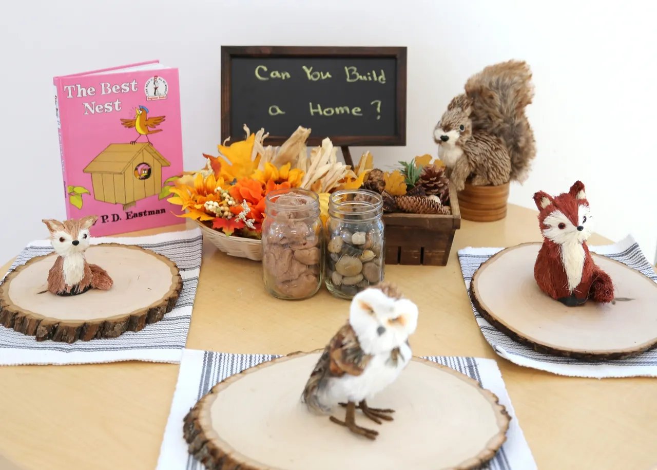 Autumn tabletop display with The Best Nest, a home-themed chalkboard, fall leaves, and small animal figurines.