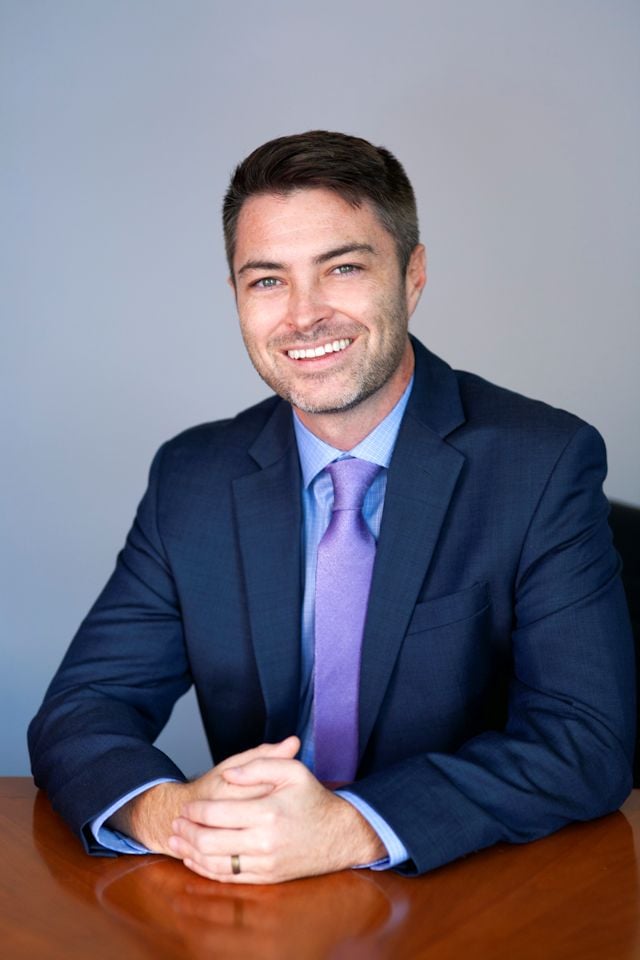 Kevin Michael Breen seated at a table in a navy suit and purple tie.