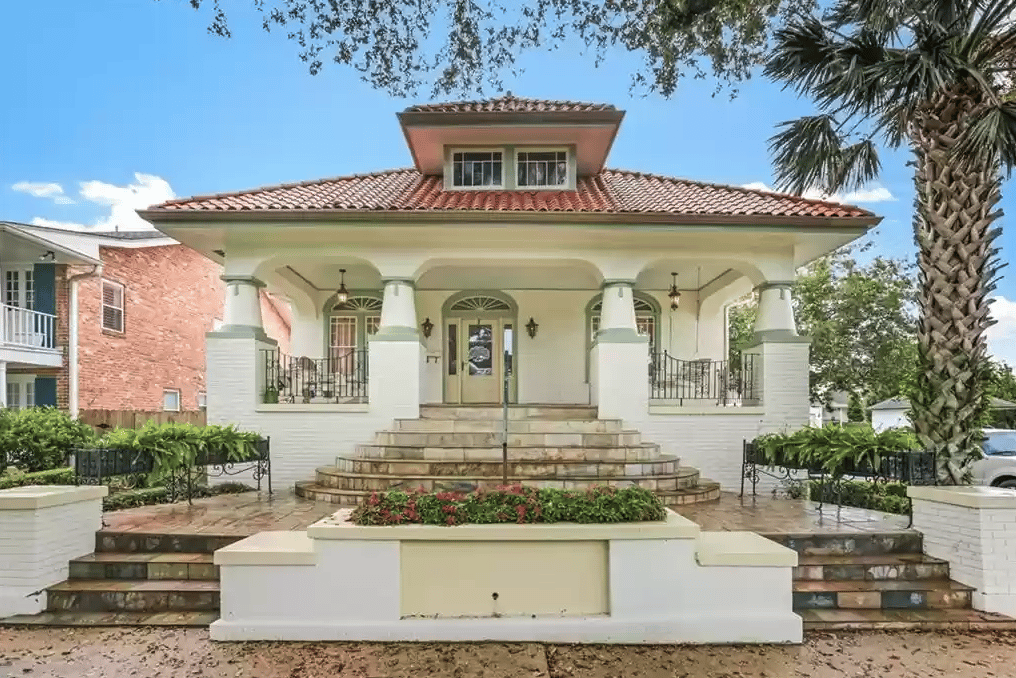 Cream house with a red tile roof, covered porch, curved steps, and a flower planter.