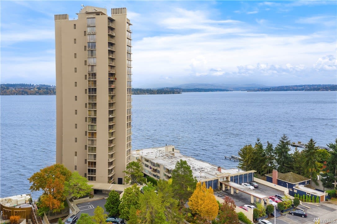 Side view of a towering lakeside luxury condo with a backdrop of overcast skies and autumn trees.