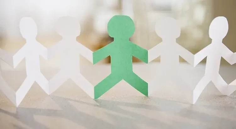 Paper cutouts of people holding hands in a line, with one figure highlighted in green. This image likely represents community, inclusion, or teamwork.