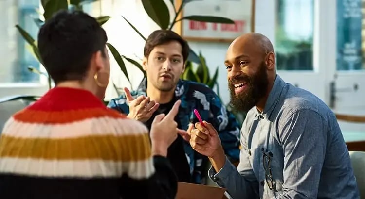  A group of people having a lively conversation at a table in what appears to be a cafe or restaurant. They are smiling and engaging with each other.