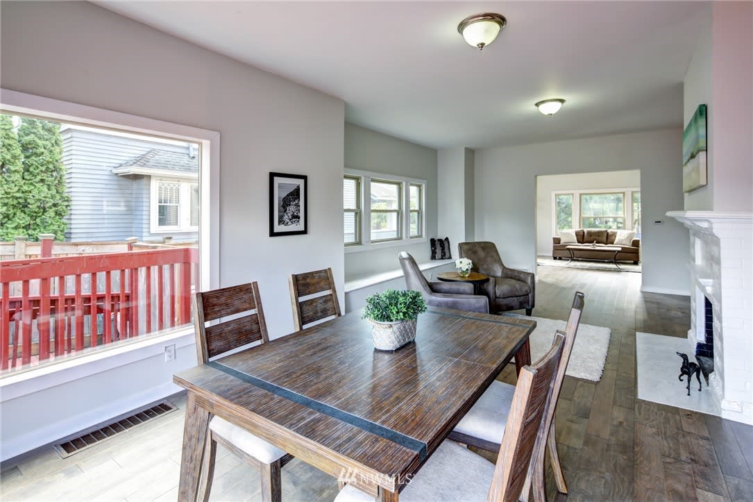 Dining room with a large wooden table, opening to a living area with a white fireplace.