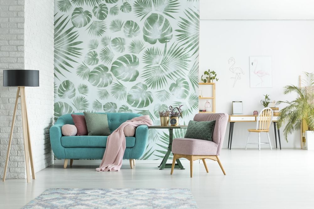 Bright living room with tropical leaf wallpaper, teal sofa, and blush armchair.