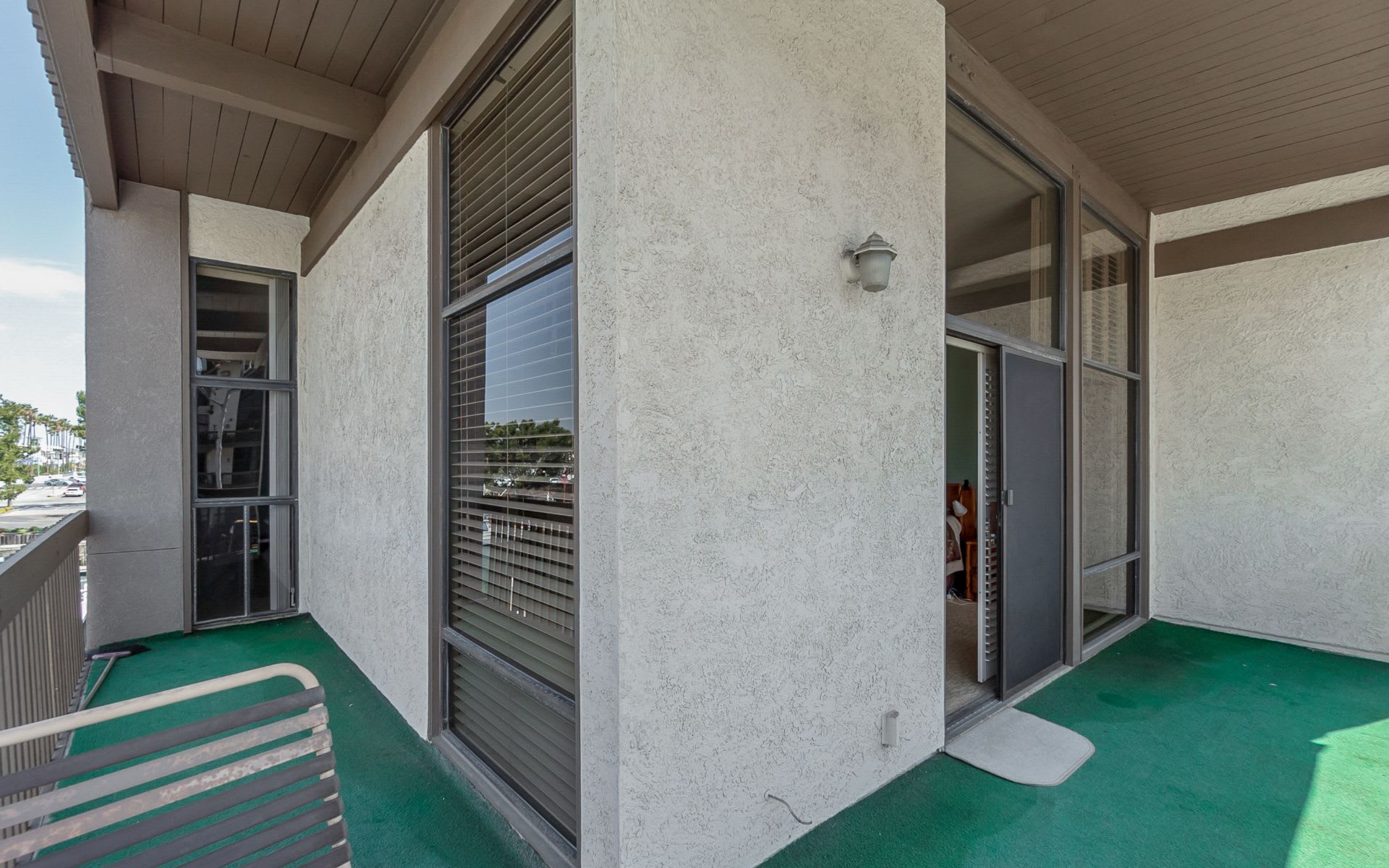 Covered balcony with green flooring, sliding glass doors, and a metal slatted bench.