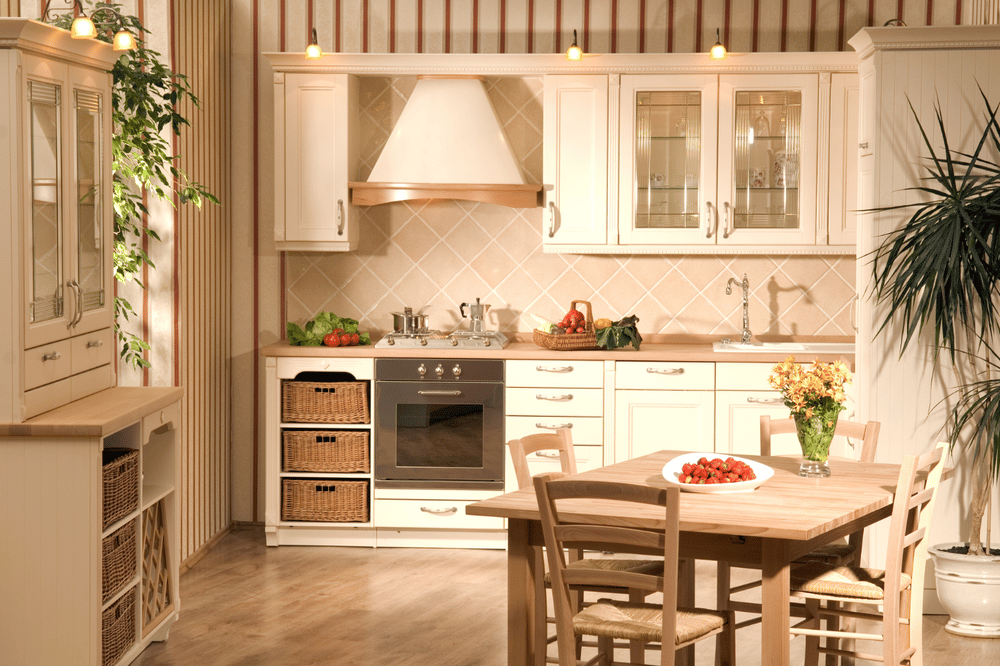 Traditional cream kitchen with a wooden dining table, fresh fruit, flowers, and potted plants.