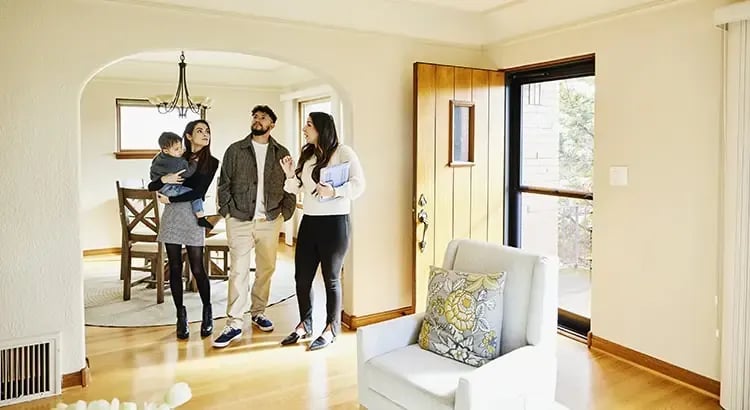 A scene inside a home, where a real estate agent is giving a tour to a couple and their child. The interior of a home, specifically the entrance area leading to the living or dining room.