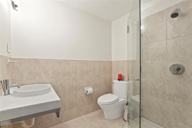 Bathroom with a wall-mounted sink, toilet, and beige-tiled glass shower.