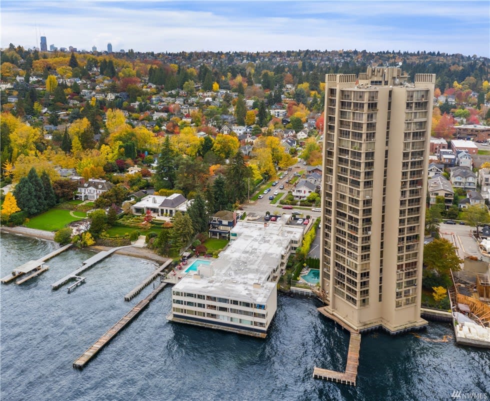 Aerial view of a high-rise luxury condo tower by the water, amidst colorful autumn foliage.