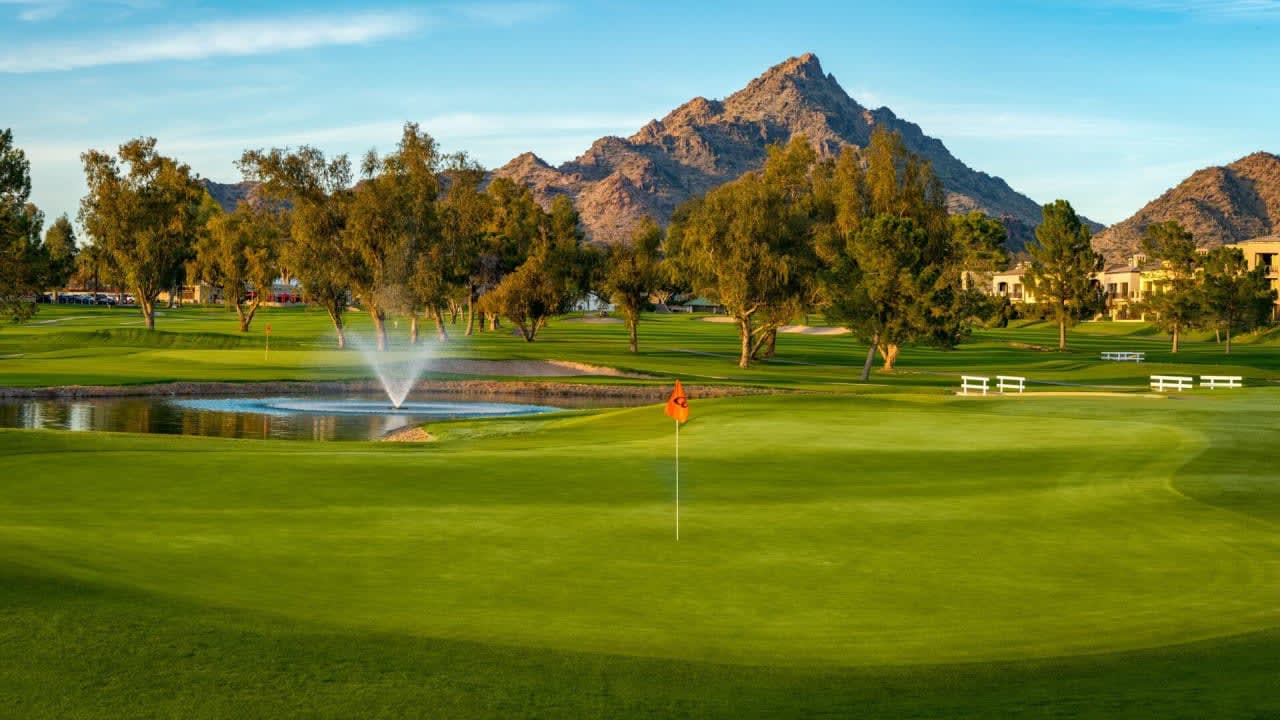 Golf course with lush fairways near luxury homes, highlighted by a tranquil fountain at golden hour.