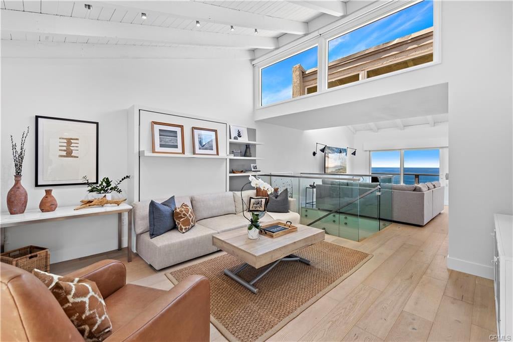 Bright living room with vaulted ceiling, glass railing, and ocean views through wide windows.