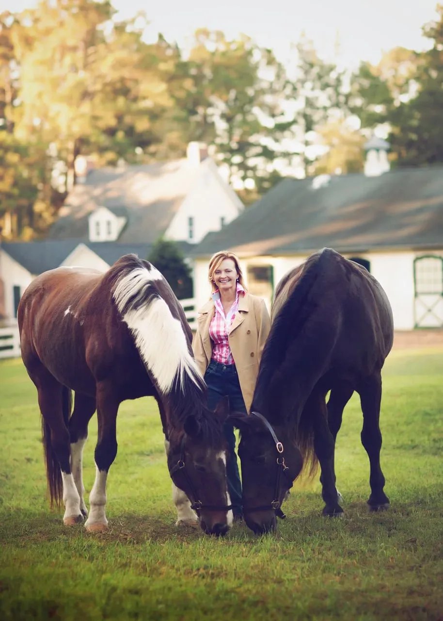 Jamie McDevitt between two horses in front of a country estate.