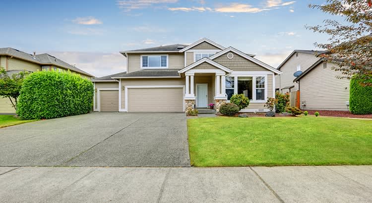 A suburban house with a well-maintained front lawn and driveway. The house looks modern and inviting, with a clear blue sky in the background, suggesting a sunny day.