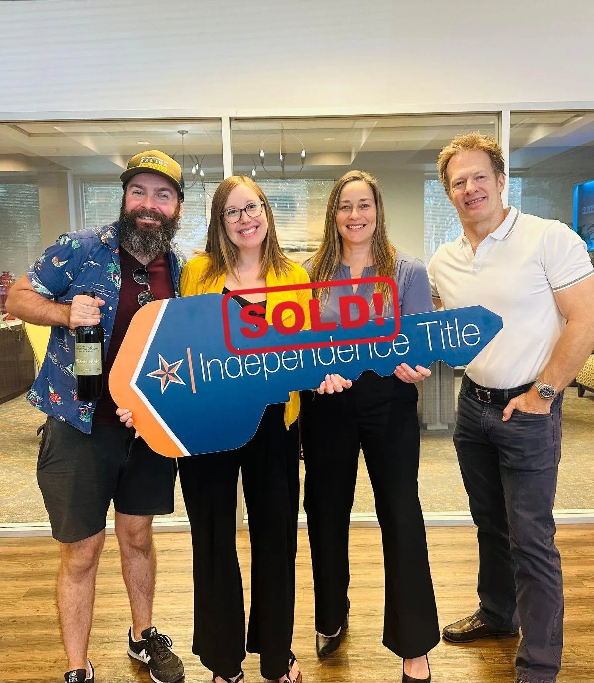 Four adults celebrate a home sale while holding an oversized SOLD key sign.