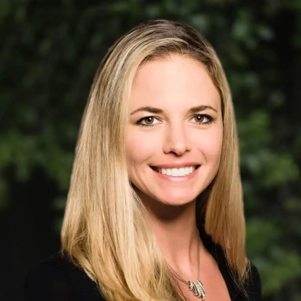 Hilary Saunders smiling in a black top against a blurred green background.