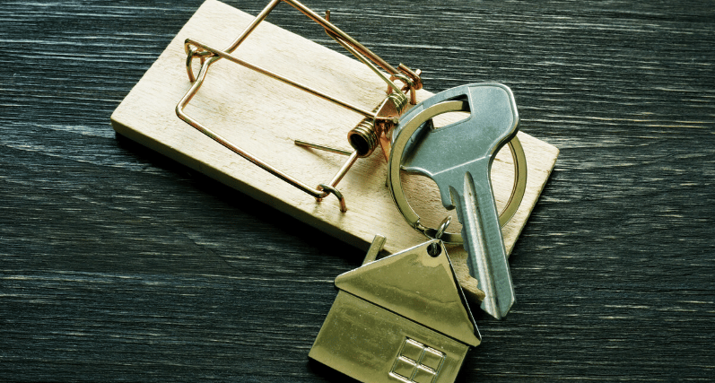 House keys and a house-shaped keychain rest on a wooden mousetrap.