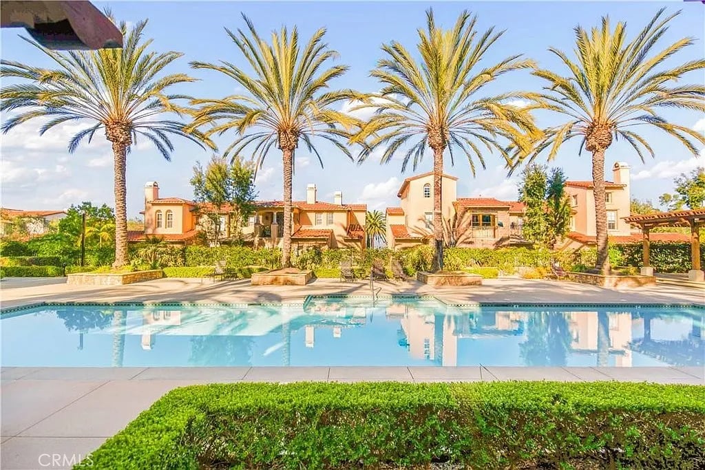 Community pool bordered by palm trees and Mediterranean-style homes.