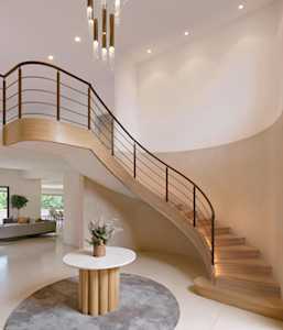 Modern foyer with a curved wood staircase, black railing, and round console table.
