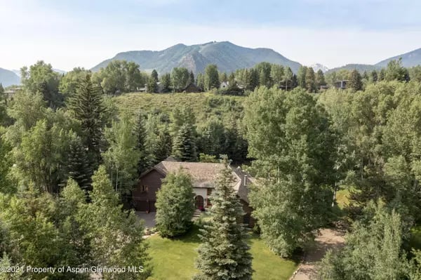 Aerial view of a home among trees, with a lawn and mountain backdrop.