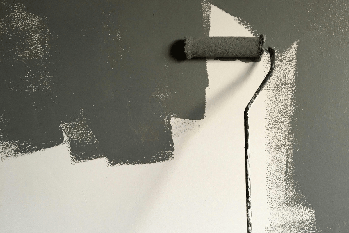 A close-up of a paint roller applying a fresh coat of dark gray paint to an interior wall, enhancing the home’s aesthetic appeal.