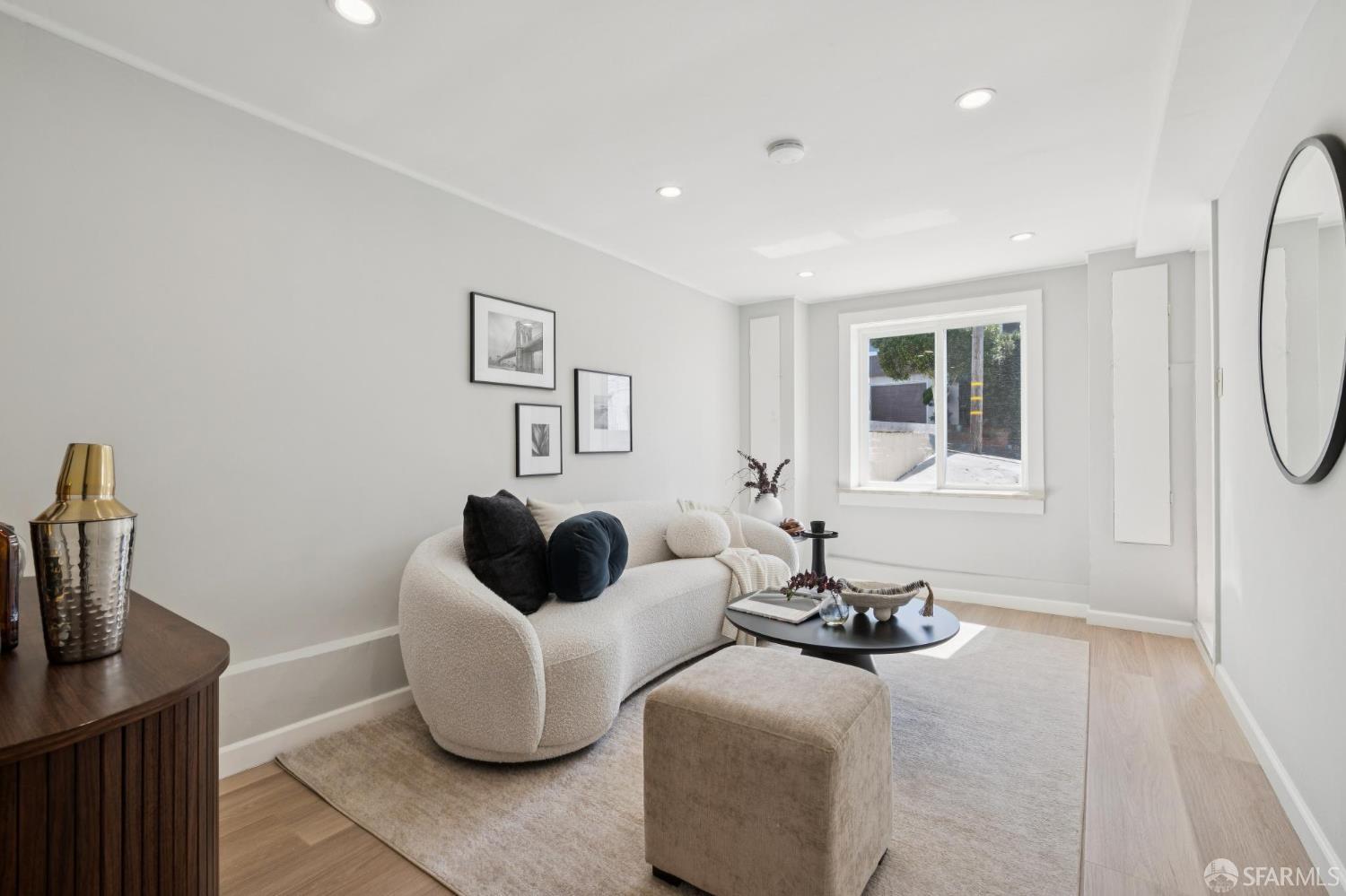 Furnished living room with a curved white sofa, round coffee table, and large window.