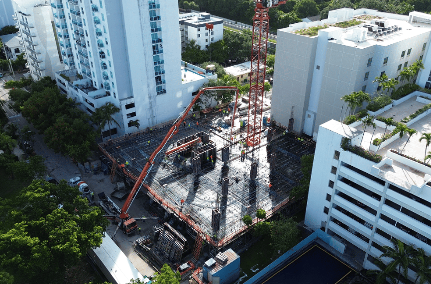 Aerial construction site with a tower crane, concrete pump, and exposed reinforcing steel.