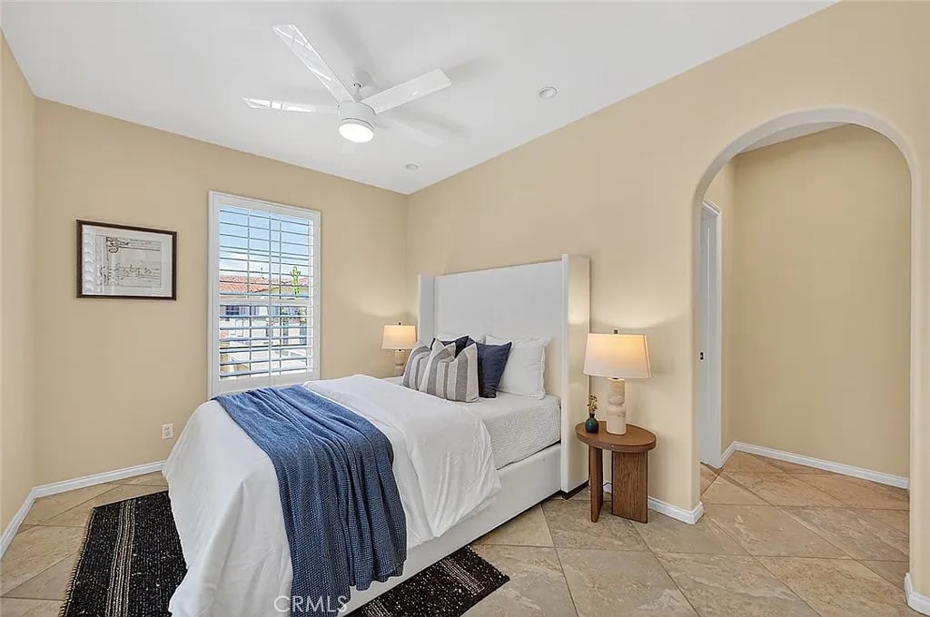 Staged bedroom with a white bed, blue throw, shuttered window, and arched doorway.