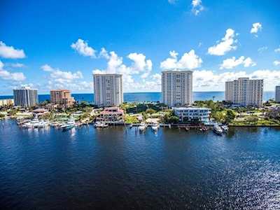 Waterfront condominiums line a blue waterway, with the ocean visible in the distance.
