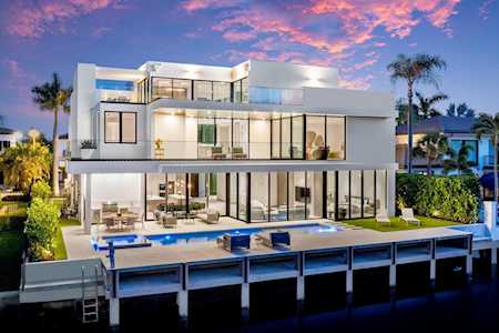 Modern glass-fronted waterfront home with a pool and dock at dusk.