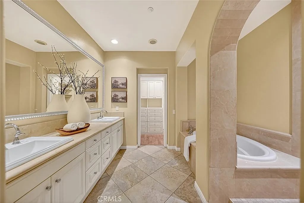 Primary bathroom with a long double vanity and soaking tub framed by a tiled arch.