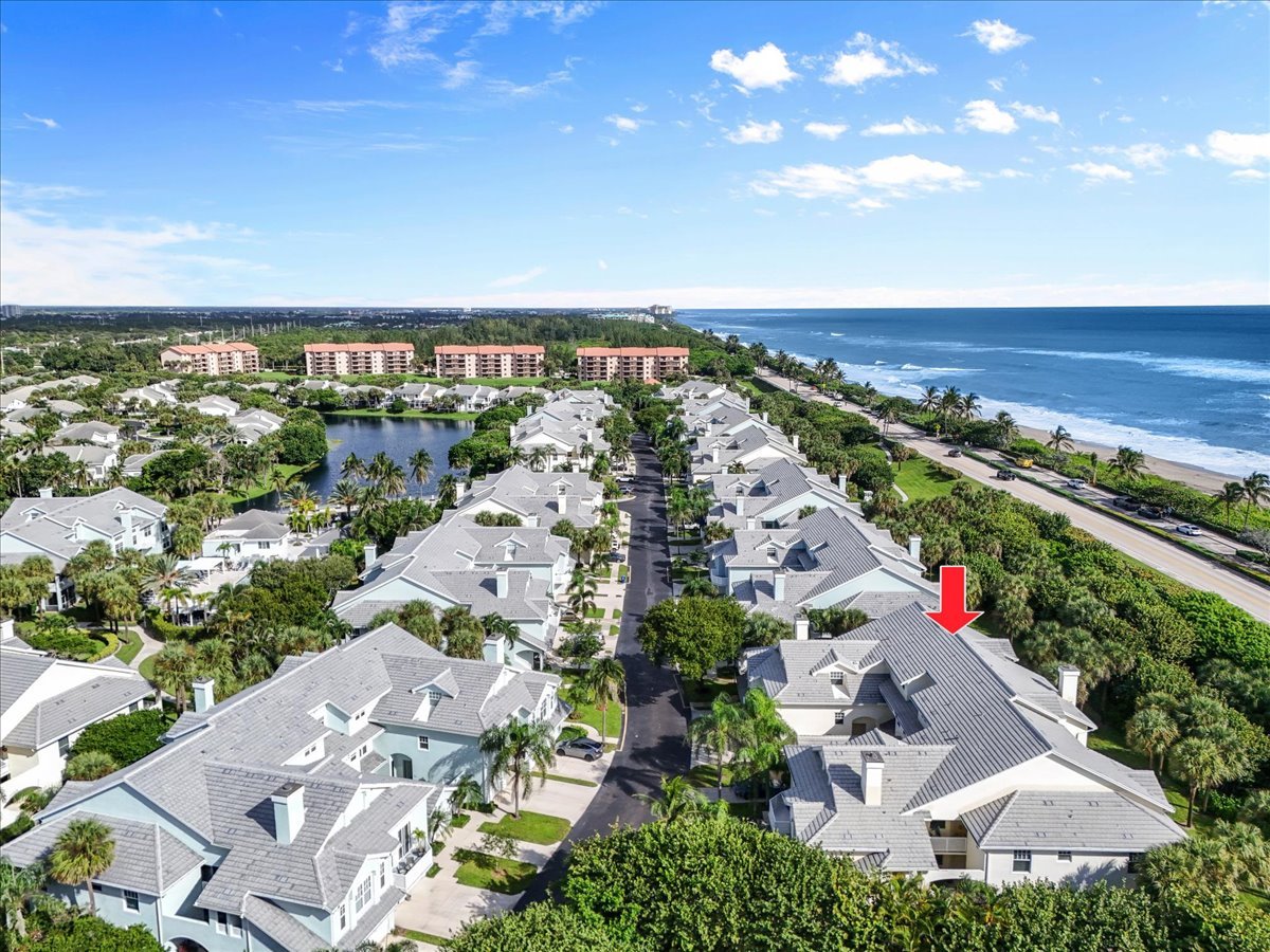 Aerial view of homes near the ocean, with a red arrow pointing to one roof.