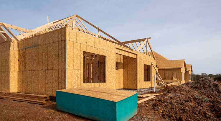 New homes under construction with wooden frames, exposed beams, and plywood siding. The scene conveys a sense of progress and development.