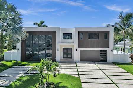 Modern two-story home with large windows, a grid-pattern driveway, and palm-framed landscaping.