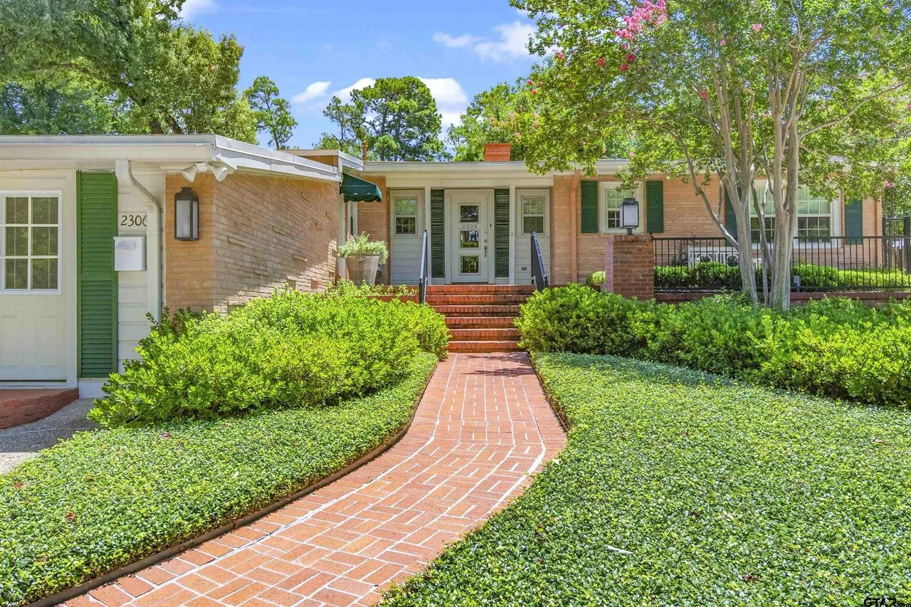showing front exterior of home with stairs to front door, green bushes, and red pavement walkway