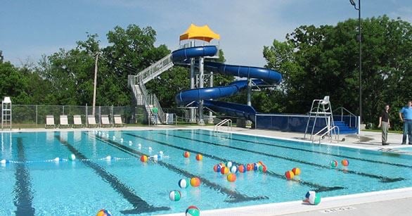Outdoor community pool with lane markers and a large blue twisting water slide.