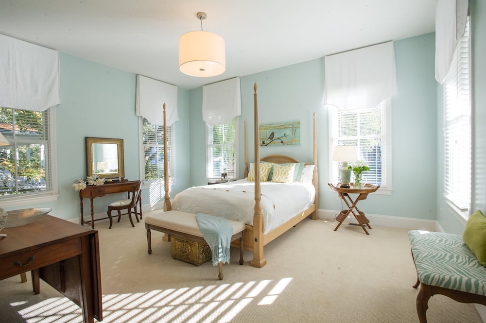Master bedroom with a four-poster bed, pale aqua walls, and sunlight streaming through tall windows.